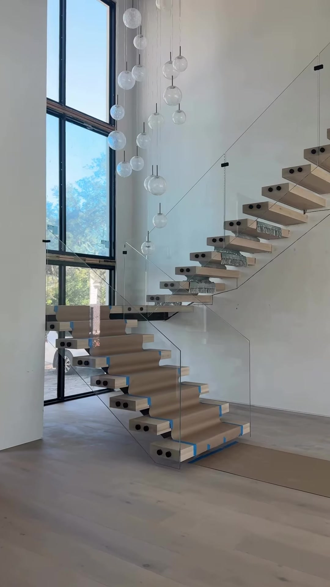White oak floating stair treads beside glass rails and tall windows
